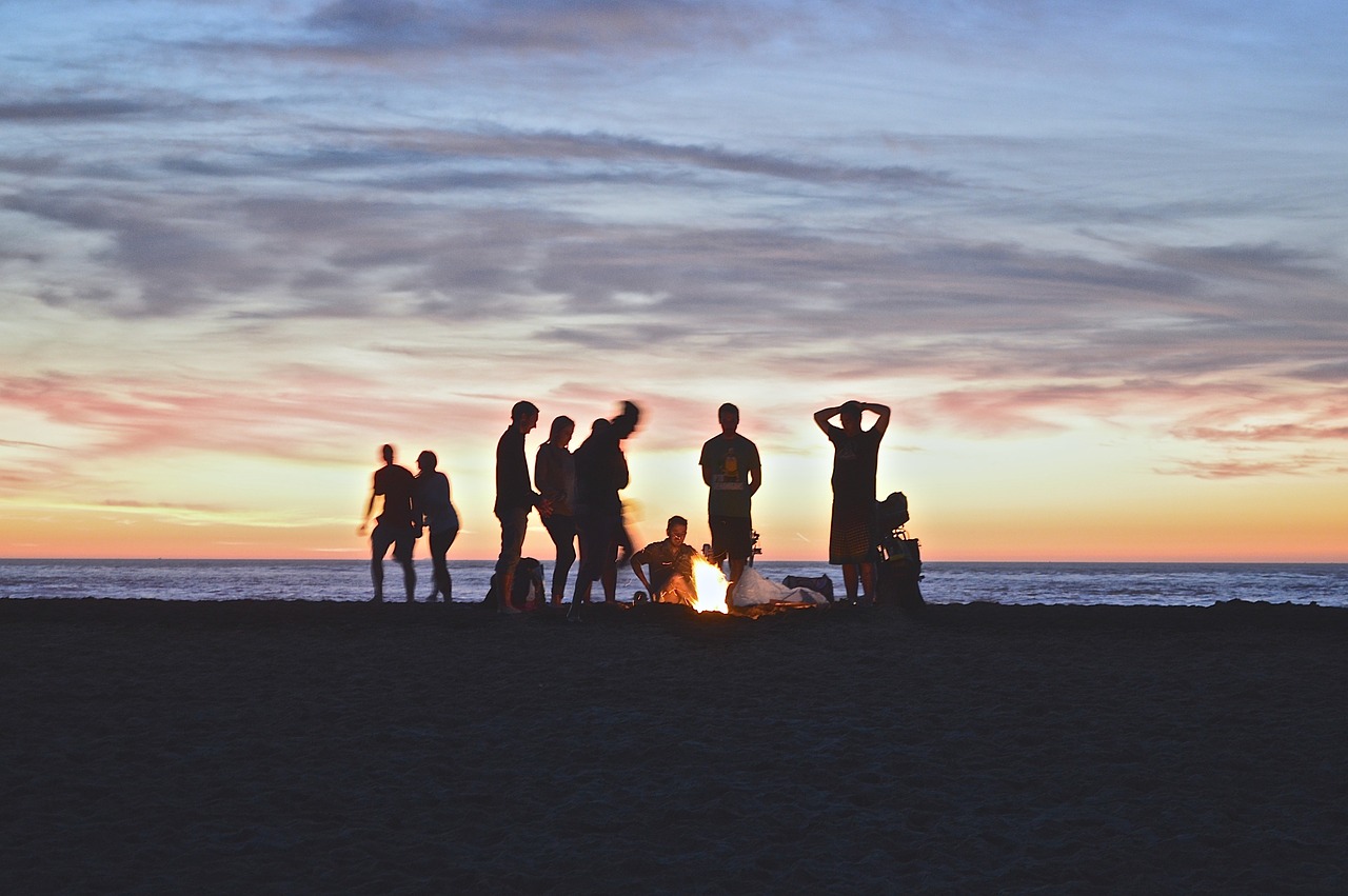 A campfire at the beach with a group of friends gathered.